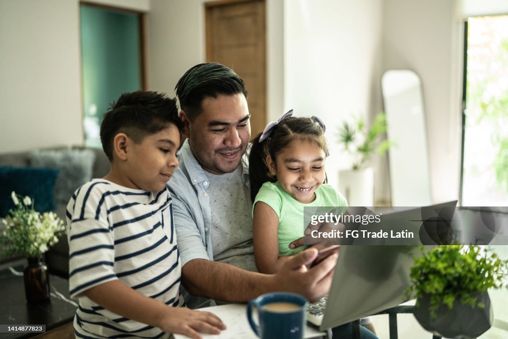 Père avec ses enfants utilisant un ordinateur portable et un téléphone portable en regardant quelque chose à la maison