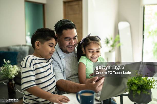 father with his kids using laptop and mobile phone watching something at home - latin american and hispanic 個照片及圖片檔