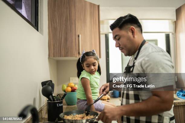 padre cocinando mientras habla con su hija en la cocina de casa - tarea doméstica fotografías e imágenes de stock
