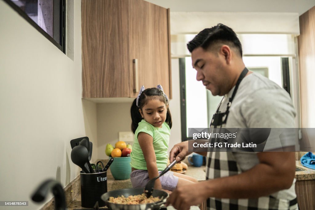 Father cooking while talking with his daughter in the kitchen at home