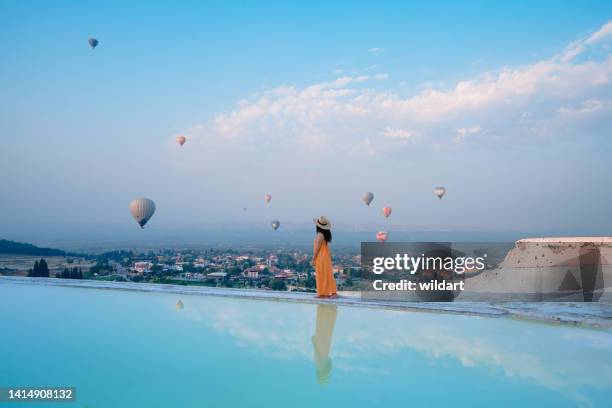 美しい旅行者の観光客の女の子は、デニズリ、トルコのパムッカレトラバーチンプールで熱気球を見ている - club nomadic ストックフォトと画像