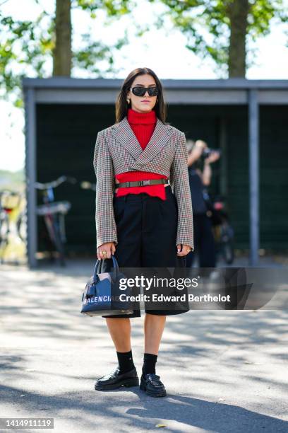 Guest wears black sunglasses, gold earrings, a red ribbed wool / turtleneck / open sides pullover, a beige / black / red checkered print pattern...