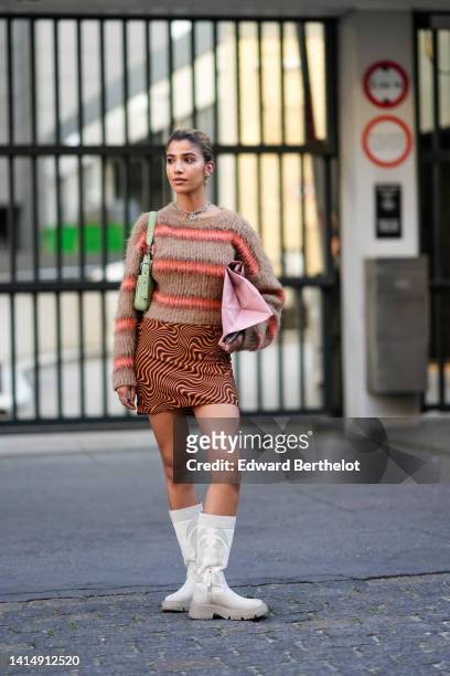 Guest wears earrings, a brown with orange striped print pattern fluffy pullover, a pale green matte leather shoulder bag, an orange and black wavy...