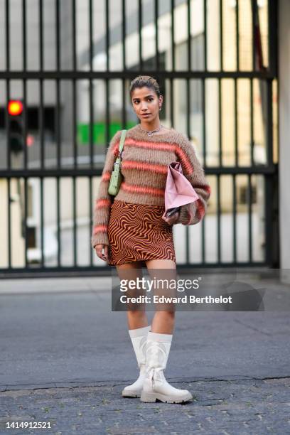 Guest wears earrings, a brown with orange striped print pattern fluffy pullover, a pale green matte leather shoulder bag, an orange and black wavy...