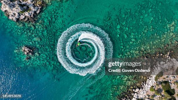 zoom arrière vue aérienne étonnante d’un homme conduisant une motomarine dans l’océan créant un motif circulaire droit vers le bas, fond d’été étonnant, couleur de l’eau et belle journée d’aventure turquoise claire sur la plage tropicale - moving image photos et images de collection