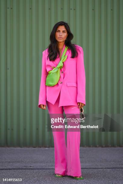 Guest wears gold earrings, a pink oversized blazer jacket, matching neon pink flared pants, a green shiny satin crossbody bag, green shiny leather...