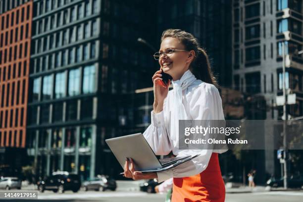 young woman with laptop talking on cell phone outdoors. - shiny hair back stock pictures, royalty-free photos & images