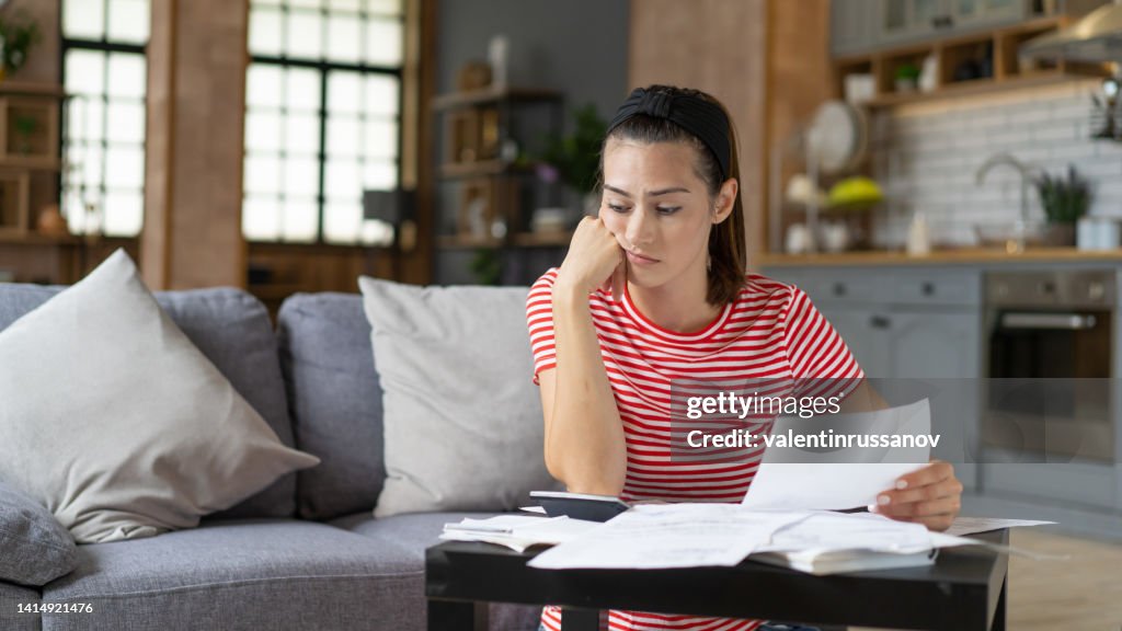 Focused millennial caucasian woman calculating domestic expenses, paying bills or taxes, planning investment or checking financial data. Life in economic inflation, dealing with financial issues.