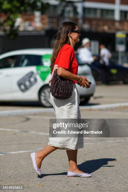 Guest wears brown sunglasses, gold earrings, a red t-shirt, a dark brown braided shoulder-bag, white latte linen midi skirt, pale purple shiny...