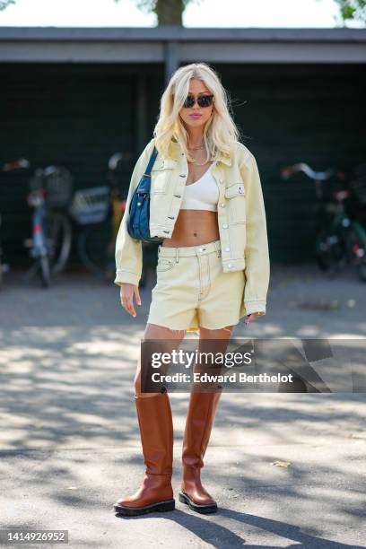 Guest wears black sunglasses from Gucci, gold earrings, a gold necklace, a white V-neck / cropped top, a blue shiny leather shoulder bag, a pale...