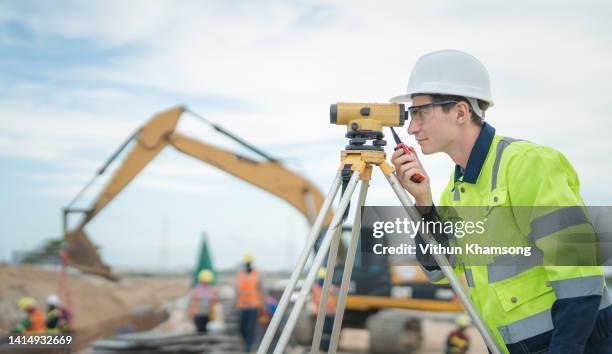 male engineer working with survey equipment on construction site and worker background - measure stock-fotos und bilder