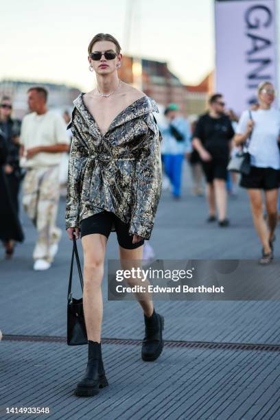 Guest wears black sunglasses, silver earrings, a silver chain necklace, a beige / brown / black shiny leather snake print pattern / shoulder-off /...