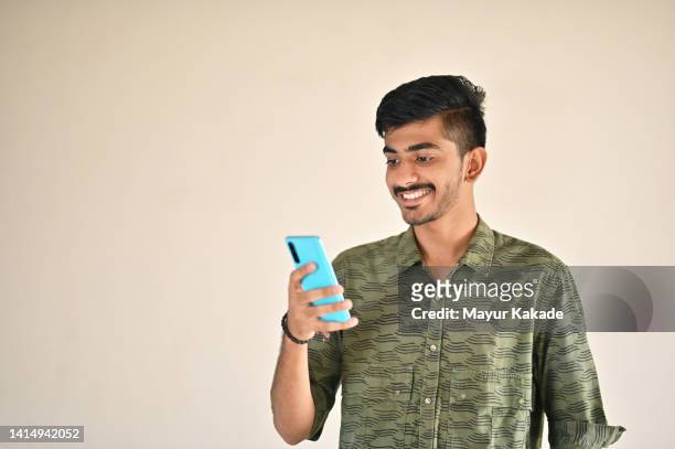studio shot of a young man looking and smiling at the mobile phone. - indian subcontinent ethnicity stock pictures, royalty-free photos & images