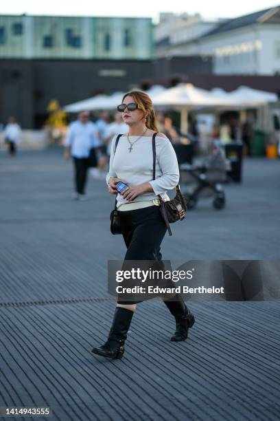 Guest wears black sunglasses from Versace, silver and pearls earrings, gold chain necklace, a white shoulder-off / long sleeves pullover, a black...