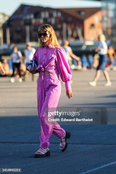 Guest wears black butterfly sunglasses, a purple pink linen puffy sleeves / knot shirt, matching purple pink linen large pants, purple matte leather...