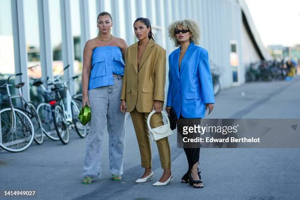 Guest wears a gold large chain necklace, a blue leather shoulder-off top, gray denim large pants, a green shiny leather handbag, green shiny strappy...