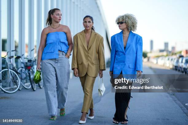 Guest wears a gold large chain necklace, a blue leather shoulder-off top, gray denim large pants, a green shiny leather handbag, green shiny strappy...