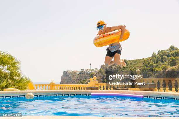 teenage boy jumping into swimming pool with a rubber ring - boy swimming pool goggle and cap stock pictures, royalty-free photos & images