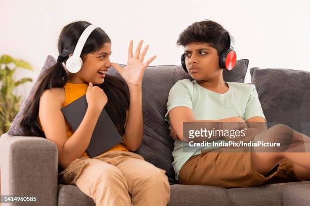 young sister teasing her brother while sitting on sofa with digital tabletin living room - annoying brother stock pictures, royalty-free photos & images
