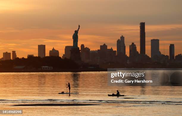 Two people paddle past the Statue of Liberty and the skyline of Brooklyn as the sun rises in New York City on August 15 as seen from Jersey City, New...