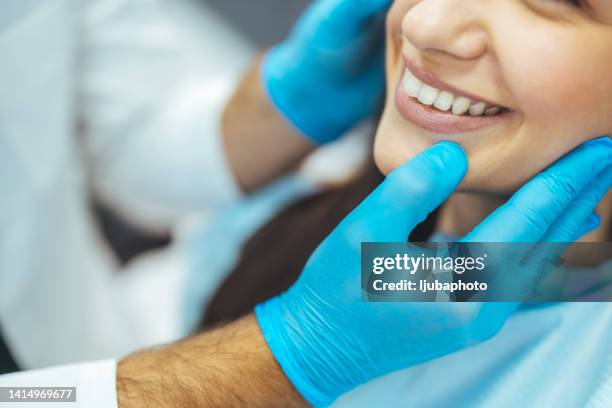cliente sonriendo mientras un dentista la examina en una clínica dental - orthodontics fotografías e imágenes de stock
