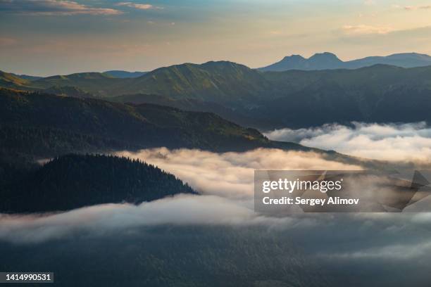 dramatic landscape of fog creeping between mountains at sunset - stratus stock pictures, royalty-free photos & images