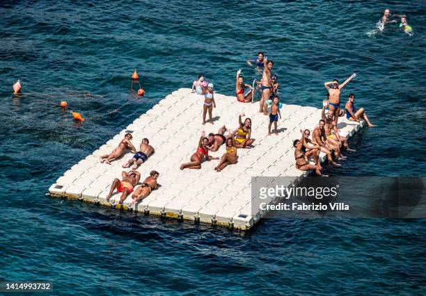Aerial view of a group of youngsters on a small platform having fun in the sea of Catania's cliffs on August 15, 2022 in Catania, Italy. 15 August is...