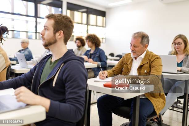 älterer schüler, der sich während des unterrichts notizen macht - mature students stock-fotos und bilder