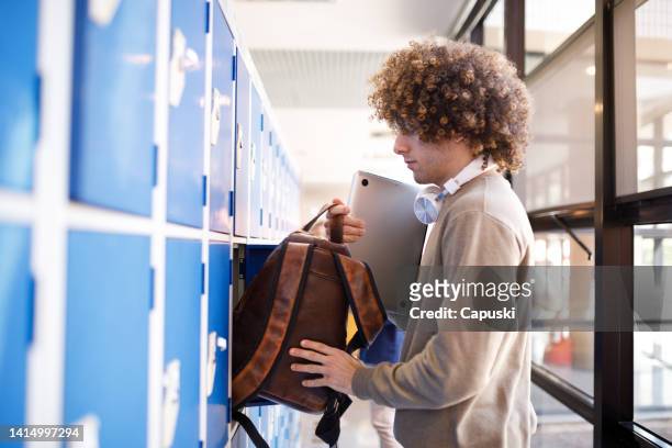 student storing his backpack inside a locker - school bag stockfoto's en -beelden