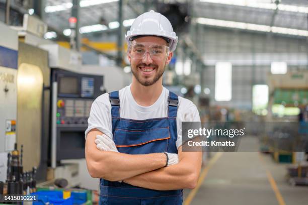 portrait of a male technician standing in factory shop floor. female in uniform looking at camera with arms crossed. - camera operator stock pictures, royalty-free photos & images