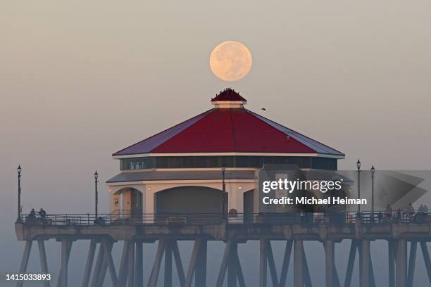 The Sturgeon Moon sets behind the Huntington Beach Pier over the Pacific Ocean on August 12, 2022 in Huntington Beach, California. The Sturgeon Moon...