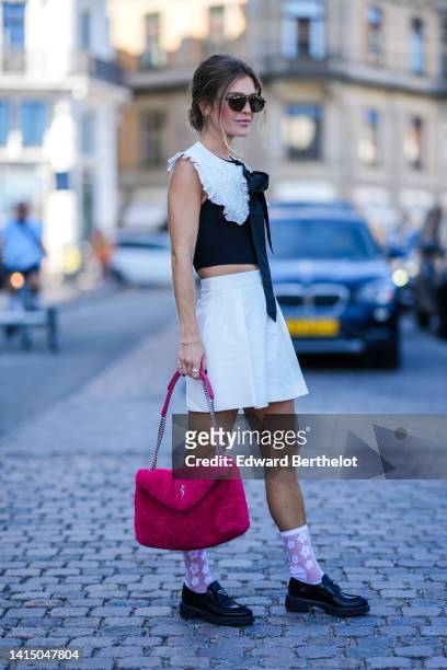 Guest wears black sunglasses, a black cropped top with an embroidered white lace print pattern oversized collar, a white pleated / accordion short...
