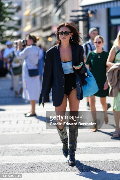 Guest wears black sunglasses, a black oversized blazer jacket, a half blue and black body, silver rings, a blue shiny leather braided large handbag,...
