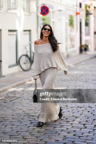 Guest wears black sunglasses, a beige wool oversized / shoulder-off / long sleeves long sleeveless, a black shiny leather Timeless handbag from...