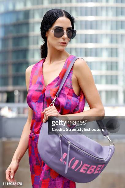 Model and artist Zoe Helali wearing a purple and pink jumpsuit with animal print by Miss Goodlife, a pastel purple back by Miss Goodlife, dark brown...