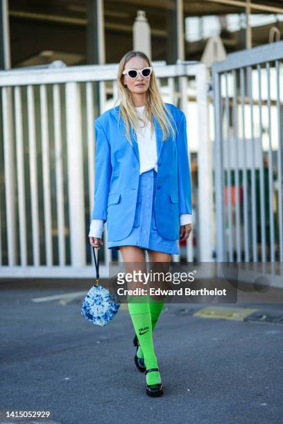 Guest wears white sunglasses, a white t-shirt, a blue blazer jacket, a blue shiny leather buttoned short skirt, a pale blue and blue tie and dye...