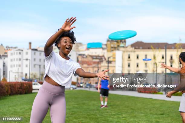 young african woman is catching a frisbee while playing with friends in a park. - frisbee stock pictures, royalty-free photos & images