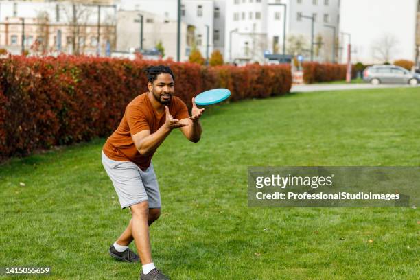 young african man is catching a frisbee while playing with friends in a park. - flying disc stock pictures, royalty-free photos & images