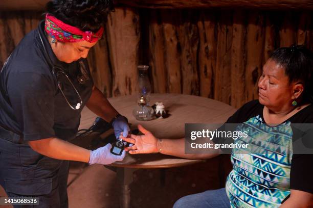 young woman, paramedic emergency medical technician, assisting her patient with monitoring her blood sugar, with a finger poke, drop of blood and a glucose monitor - diabetes and heart disease stock pictures, royalty-free photos & images