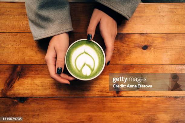 woman hands hold a ceramic cup with matcha green tea latte with foam art on the wooden table. backdrop for your design with copy space. photography from above - tea cup overhead view photos et images de collection