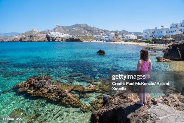 woman looks out to town from rock outcrop above sea - naxos stockfoto's en -beelden