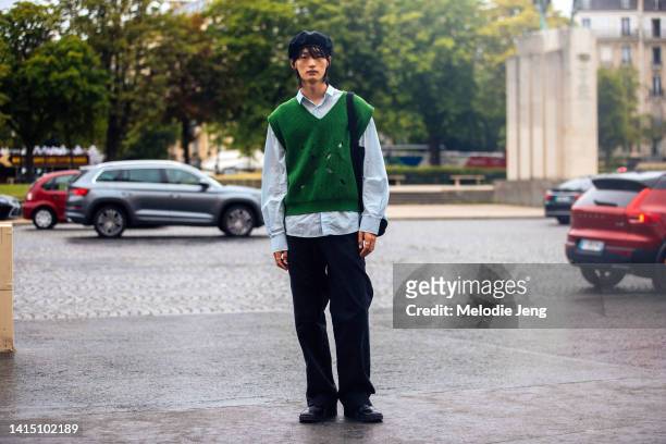 Model Seungchan Lee wears a black beret, green knit vest over a blue shirt, black pants, black boots after the Craig Green show at Musée de l'Homme...