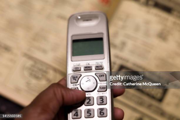black woman holding traditional cordless telephone with classified pages in phone directory in background - landline phone home foto e immagini stock