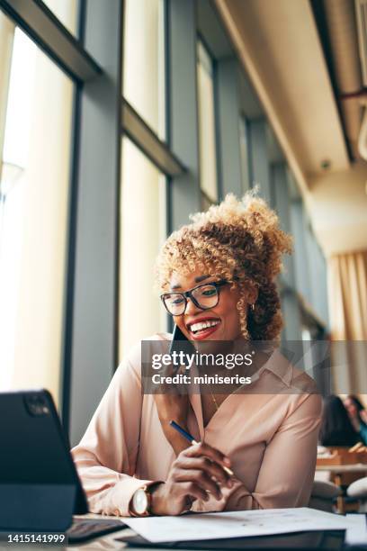 smiling businesswoman talking on a mobile phone in the cafe - friendly business phonecall stockfoto's en -beelden