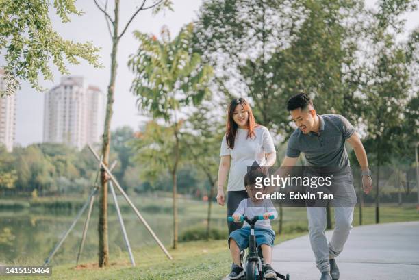 asian chinese boy learning cycling in public park with his 2 parents during weekend morning - asian young family stockfoto's en -beelden