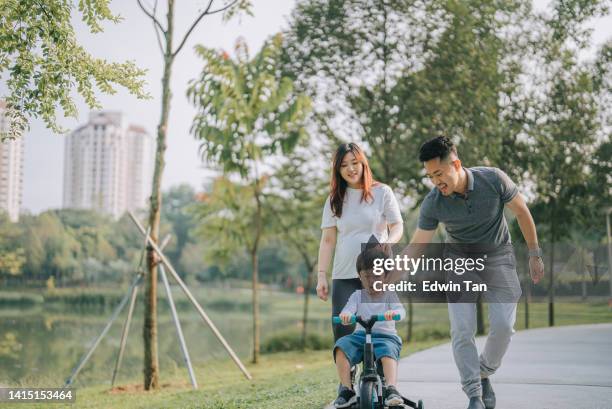 asian chinese boy learning cycling in public park with his 2 parents during weekend morning - asian cycling stock pictures, royalty-free photos & images