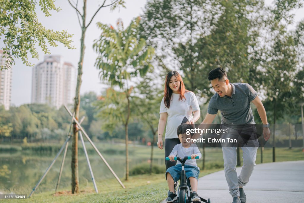 Menino chinês asiático aprendendo ciclismo em parque público com seus 2 pais durante a manhã de fim de semana