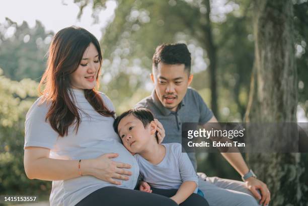 asian chinese boy listening to his little sister heartbeat leaning  mother abdomen  bonding time with her husband and son sitting on park bench in the morning - little kids belly imagens e fotografias de stock