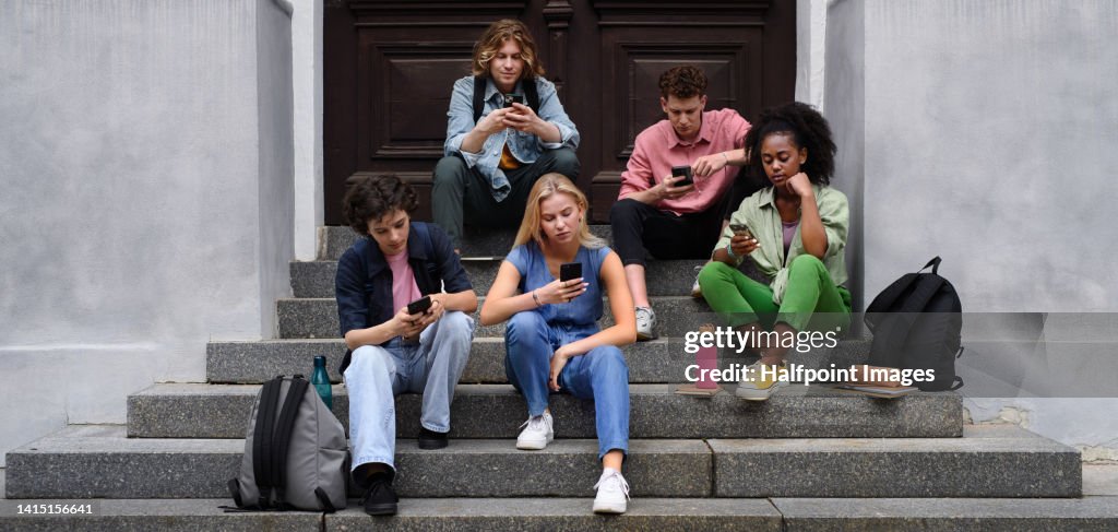 Group of teenagers sitting in outdoor stairs in front of school.
