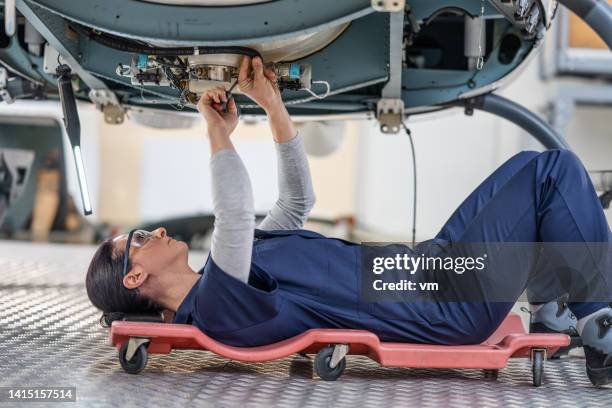 female aviation mechanic in uniform lying on cart on wheels and repairing helicopter - jet lag stockfoto's en -beelden